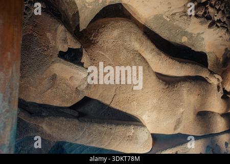 Ajanta, India - 26 dicembre 2025: Veduta di un colossale Buddha sdraiato scolpito nelle pareti della grotta, la sua forma che emerge dalla pietra nel tono della terra Foto Stock