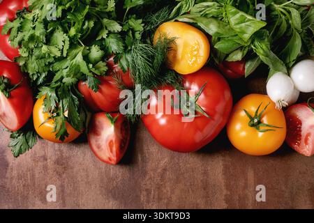 Verdure fresche e colorate con erbe sparsi su un tavolo di legno. Pomodori peperoni cipolle prezzemolo basilico aneto disposti naturalmente. Prodotti biologici sani Foto Stock