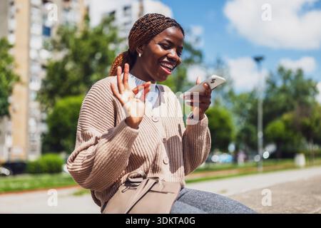 La giovane donna nera felice sta usando lo smartphone. Sta ridendo mentre registra un messaggio vocale. Foto Stock