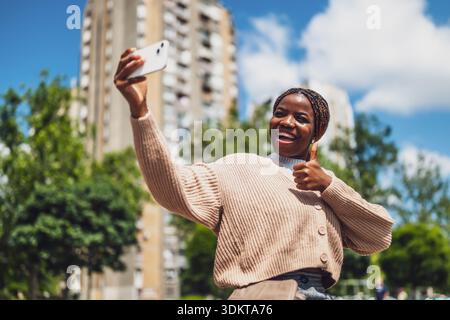 La giovane Happy Black Woman sta scattando selfie nelle giornate di sole con il suo smartphone. Foto Stock