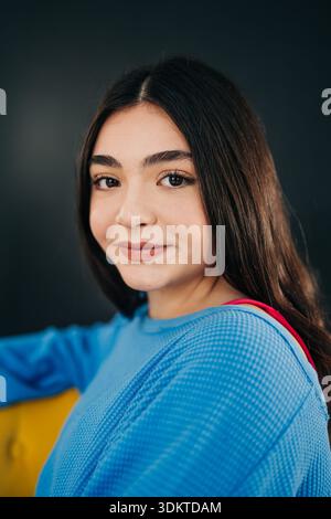 Giovane donna sorridente in maglione blu seduta su una sedia gialla Foto Stock