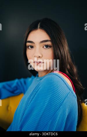Giovane donna sicura di sé in cima blu seduta su una sedia gialla Foto Stock