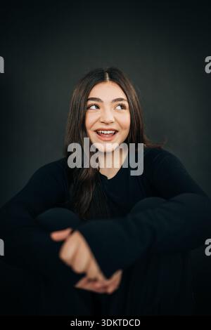 Ridendo giovane donna in abito nero seduta con le braccia incrociate Foto Stock