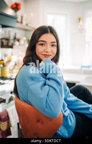 Giovane donna che indossa una felpa blu sorridente in cucina a casa Foto Stock