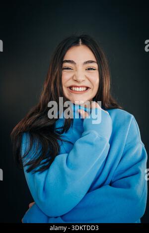 Giovane donna sorridente mentre indossa una felpa blu Foto Stock