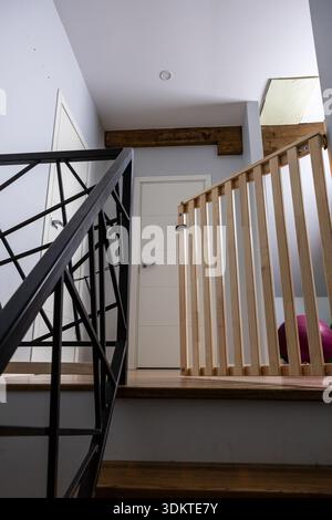 Scala interna con ringhiera in metallo nero con motivi geometrici, ringhiera in legno con spranghe verticali e porta bianca incorniciata in legno. Foto Stock