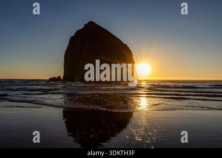 USA, Oregon, sole che sorge dietro la roccia di fieno a Cannon Beach Foto Stock