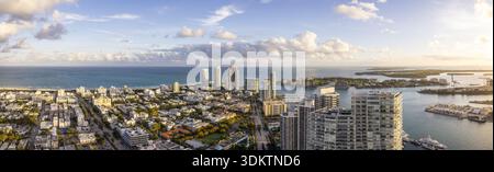 La vista aerea degli edifici baciati dal sole incontra l'oceano turchese, dove lo skyline si erge alto su una tela di cieli pastello, South Beach e Miami Beach Foto Stock