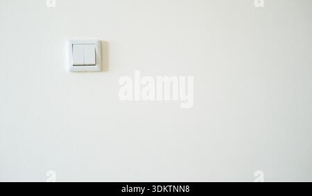 Interruttore luce a bilanciere doppio rettangolare con telaio in plastica bianca su parete in gesso bianco testurizzato; illuminazione interna piatta, vista frontale, ombre minime Foto Stock