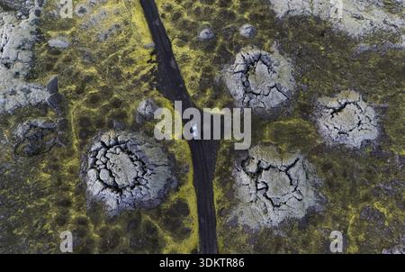 Vista aerea di tumuli muschiati, terra incrinata e un'auto solitaria che si snoda attraverso il paesaggio aspro di Selfoss, Islanda. Foto Stock