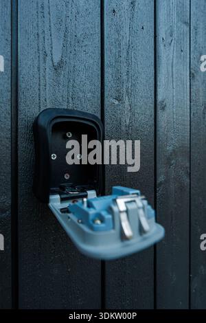 Una scatola portachiavi combinata montata è aperta su legno verniciato, mostrando un interno e un dispositivo di chiusura vuoti, corpo grigio blu, linguette cromate e viti in luce soffusa Foto Stock