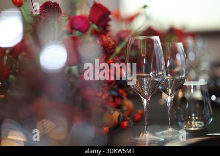 Bicchieri da vino in cristallo vuoti che riflettono la luce sul tavolo scuro, caratterizzati da un bellissimo centro floreale rosso che crea un'atmosfera da festa, raffinata Foto Stock