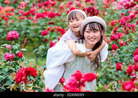 Madre che dà a sua figlia un giro in un roseto Foto Stock