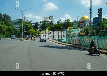 Batam, Indonesia, 1° febbraio 2026: Strada trafficata con moschea, traffico e murales colorati in un ambiente tropicale. Foto Stock