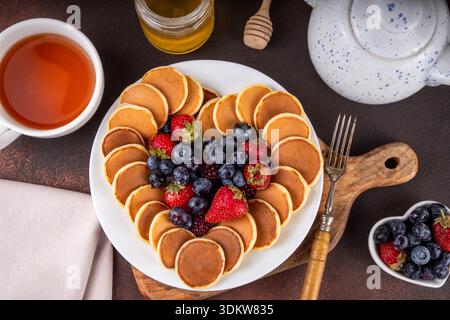 Il giorno di San Valentino, i pancake per la colazione erano carini, semplici e disposti a forma di cuore, con lampone, mirtillo e miele freschi, con tazza da tè e teiera, poliziotto Foto Stock