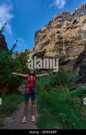 Escursionista con le braccia allungate saltando sul sentiero della gola di Masca circondato da vegetazione lussureggiante e scogliere torreggianti Foto Stock