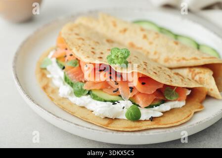 Frittelle di farina d'avena con salmone leggermente salato, cetriolo, verdure e formaggio spalmabile su piatto su sfondo chiaro, primo piano Foto Stock