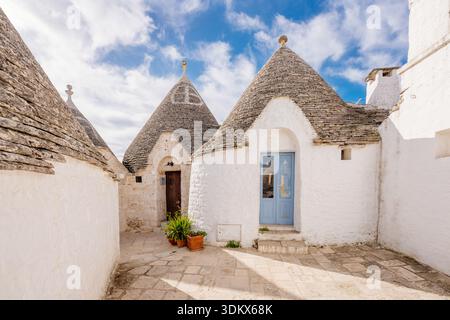 Alberobello, Italia: Case storiche Trulli su una strada affascinante sotto il cielo blu Foto Stock