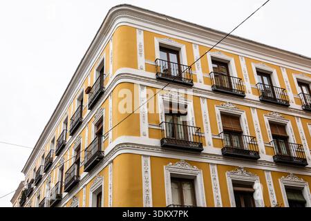 Edificio residenziale di Madrid caratterizzato da una facciata gialla, balconi e dettagli architettonici decorativi bianchi contro un cielo limpido. Mercato residenziale i Foto Stock