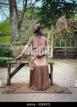Una statua arrugginita in acciaio corten della suffragetta militante Emily Wilding Davison dello scultore Ray Lonsdale seduta su una panchina a Carlisle Park, Morpeth, Foto Stock