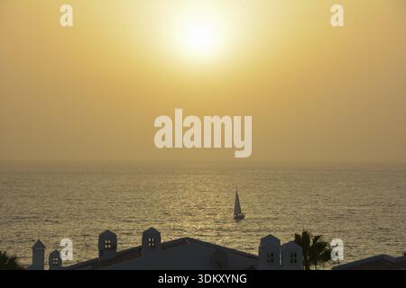 Vista del complesso di bungalow sul mare con una barca a vela al tramonto, a Costa Adeje, Spagna, Tenerife, Adeje, Spagna Foto Stock