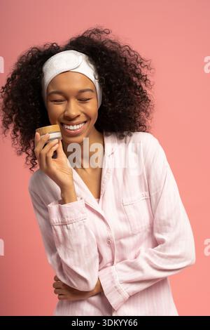 Questa giovane donna gioiosa in morbido pigiama che assapora una routine di cura della pelle trasuda bellezza e felicità. Foto Stock