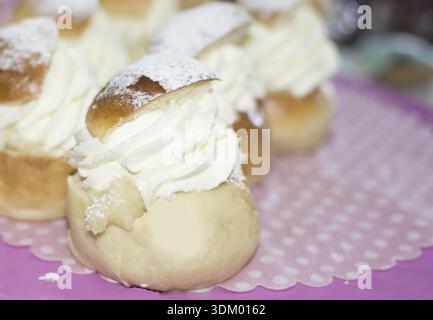 Tipici panini svedesi a febbraio - semla - con panna montata su carta tratteggiata rosa e bianca e cakeplate rosa Foto Stock