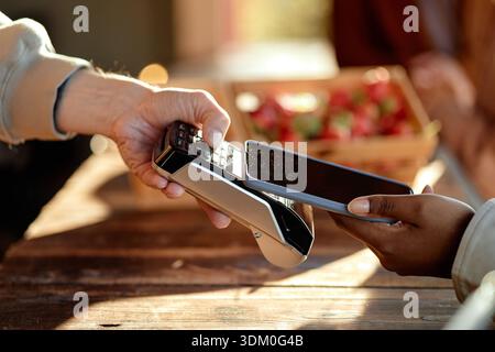 Donna nera che paga con smartphone mentre uomo caucasico che tiene in mano un lettore di carte Foto Stock