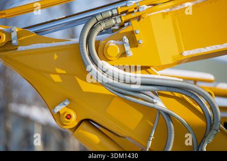 Vista dettagliata delle tubazioni idrauliche delle attrezzature da costruzione sul braccio giallo, manicotti flessibili in metallo e connettori, manutenzione di macchinari industriali Foto Stock