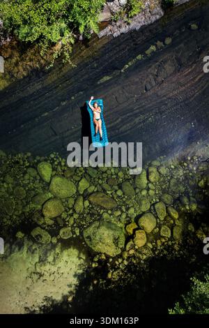 Vista aerea di una persona che galleggia su una zattera blu in un fiume limpido, il sole che si riflette sulla superficie dell'acqua, Chisa, Corsica, Francia. Foto Stock