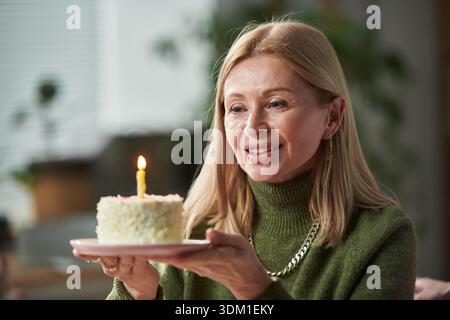Donna adulta che sorride mentre tiene la torta di compleanno con candela Foto Stock
