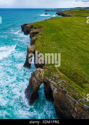 Vista aerea delle formazioni rocciose della cattedrale incontra il mare turbolento, dove la schiuma bianca contrasta con le lussureggianti scogliere verdi, Praia das Catedrais, Lu Foto Stock