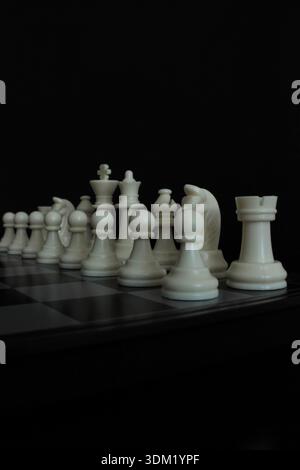 Scacchiera su sfondo nero con pezzi bianchi disposti sulla scacchiera, simboleggiando strategia, leadership e competizione intellettuale. Foto Stock