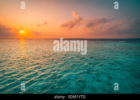 Trascinante tramonto, il sole che cala su un mare tropicale calmo e un orizzonte di barriera corallina. Oceano caldo e luminoso. Vacanza estiva, viaggio, paradiso, luna di miele scenografica Foto Stock