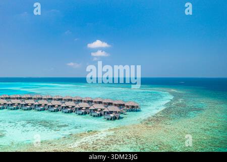 Radiose ville aeree sull'acqua delle Maldive, isola turchese, paradiso mozzafiato, resort costiero di lusso. Baia tropicale della barriera corallina Foto Stock