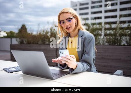 Giovane donna d'affari che lavora in multitasking all'aperto con smartphone e notebook Foto Stock