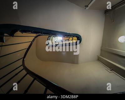 Scala a spirale all'interno di un edificio di Parigi, vista dal basso con una ringhiera di metallo scuro che si arriccia verso l'alto verso un luminoso lucernario. Un simbolo di reale Foto Stock