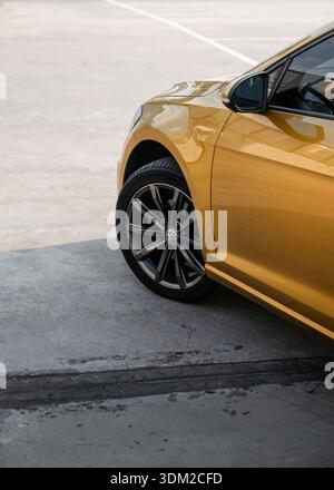 Vista laterale ravvicinata del VW Golf giallo ambra: Ruota anteriore, parafango, portiera e specchietto laterale della berlina compatta. Foto Stock