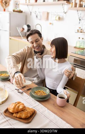 Una coppia gioiosa si siede vicino al tavolo della cucina, condividendo una deliziosa colazione con le risate. Foto Stock