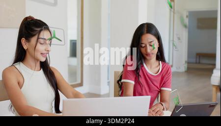 Lavorate due donne che utilizzano notebook in ufficio, indossano una maglietta senza maniche e una suoneria con sovrapposizioni AR Foto Stock