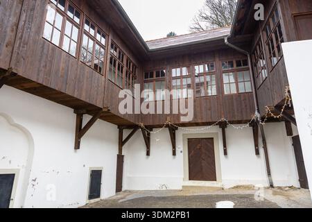 Un affascinante cortile rustico presenta una facciata di legno scuro a due piani con molte finestre, pareti in gesso bianco e luci a corda. Perfetto per lui Foto Stock