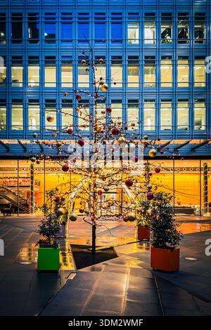Festeggia l'albero di Natale con baule rosse, dorate e verdi nella piazza del cortile centrale di Saint Giles, moderno edificio di vetro blu a Londra Foto Stock