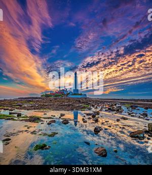 Una vista all'alba in estate del faro di St Mary vicino a Whitley Bay nel North Tyneside con la bassa marea, con un'incantevole alba colorata e il cielo Foto Stock