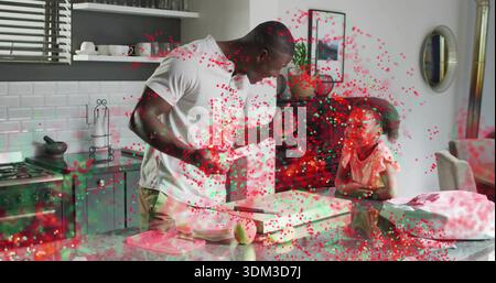 Preparare papà e ragazza all'isola della cucina, tenendo il coltello con la pera, in abito rosa, coriandoli rosso-verde Foto Stock
