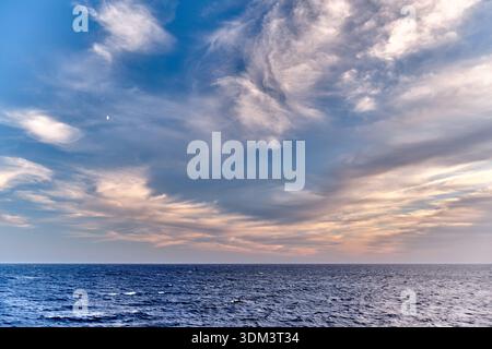 Una scena tranquilla si sviluppa sul Mar Mediterraneo vicino a Minorca. Le acque blu scuro si estendono fino all'orizzonte sotto un vasto cielo pieno di morbidi e molli c Foto Stock