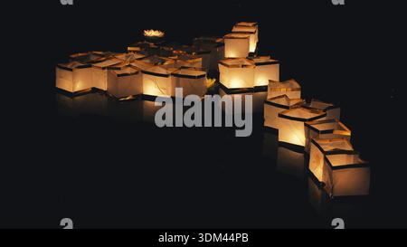 Persone che inviano lanterne di carta scintillanti su un fiume scuro e riflettente durante un festival notturno. Foto Stock