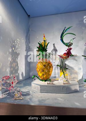 Londra, Regno Unito, 5 dicembre 2025, collezione di statuette in cristallo con ananas giallo oro con foglie verdi, uccello colorato, fiori su bianco Foto Stock