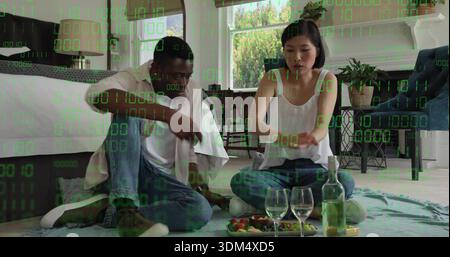 Una coppia seduta che condivide frutta e vino sulla coperta a casa, indossa jeans, rivestimento binario verde Foto Stock