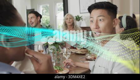 Tenendo in mano un bicchiere di vino, l'uomo adulto sulla destra reagisce al tavolo da pranzo di casa con copertura a onde punteggiate Foto Stock