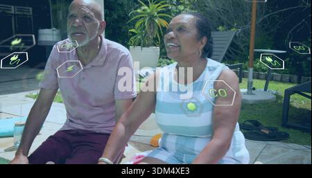 Una coppia senior seduta con una polo rosa e un prendisole a righe sul patio piastrellato, che mostra le icone dell'energia Foto Stock